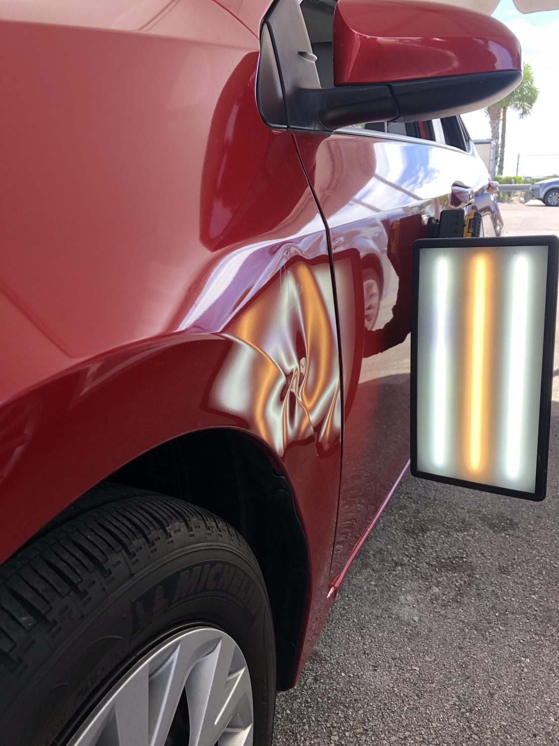Dent in a red fender shown under a PDR reflection board, Miami