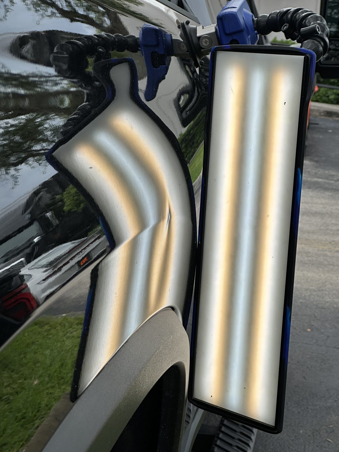 Door ding on a black panel under a PDR reflection board, Miami