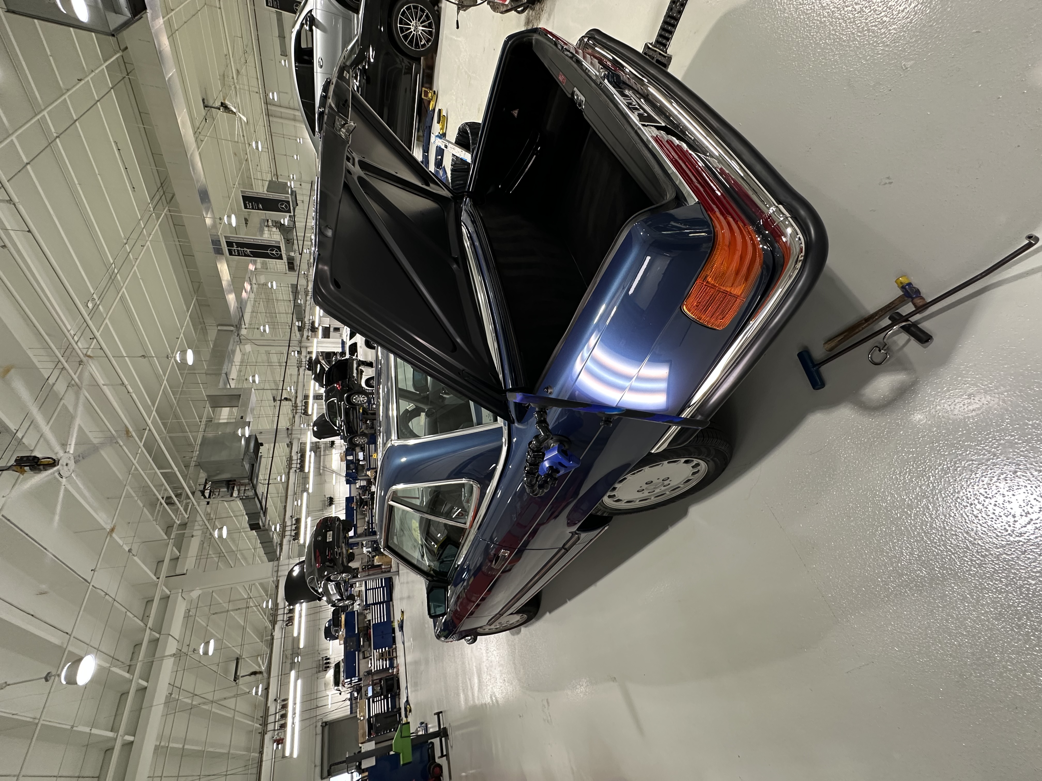 Classic navy sedan in the shop for paintless dent repair, trunk open with PDR light, Miami